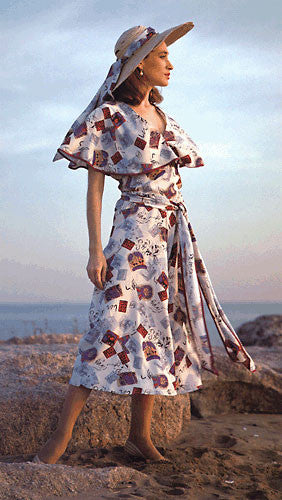 Photo of woman in shin length beach pyjamas. Standing on rocks with ocean behind her. wearing large hat with sash.