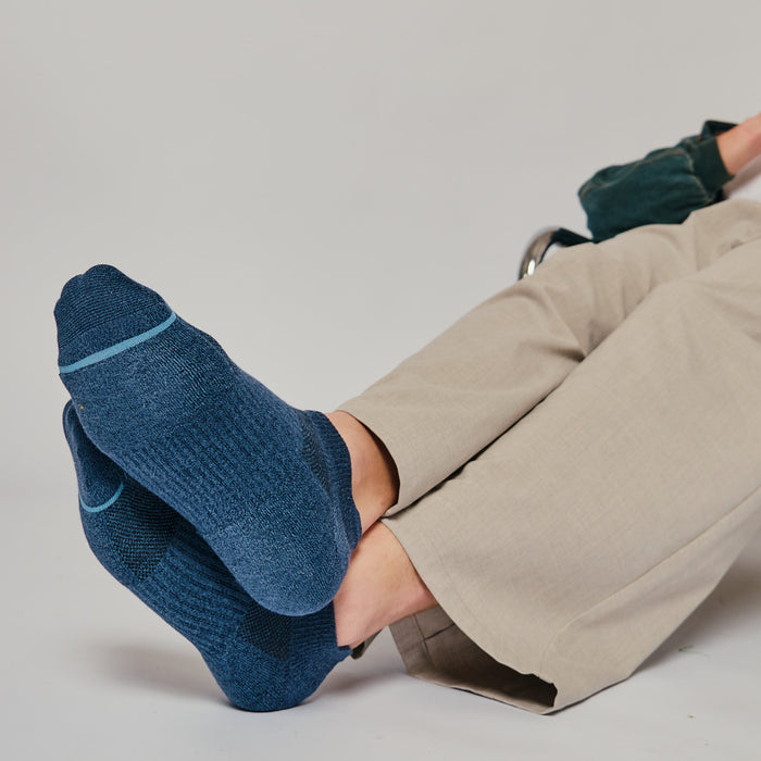 Navy ankle compression socks with a textured design and light blue accents, worn by a person seated.