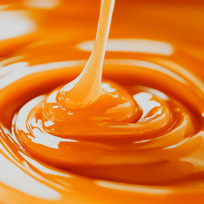 A close-up image of caramel syrup being drizzled into a pool of caramel liquid, showing a smooth, glossy texture.