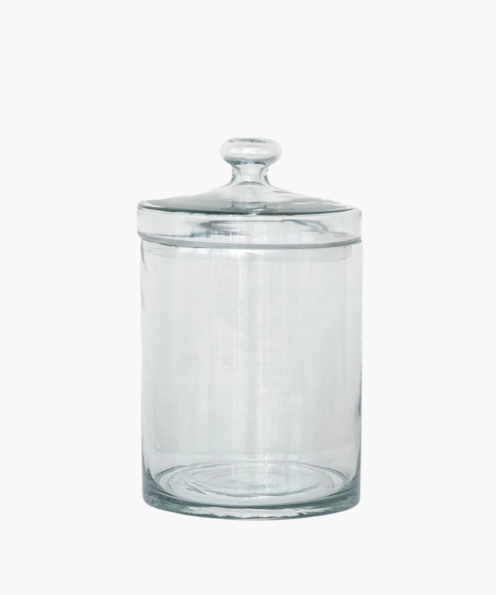 A transparent glass jar with a rounded lid is centered on a white background. The jar is empty and reflects light softly, conveying simplicity and elegance. | Wildwood Home Co.