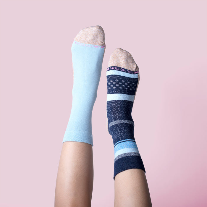 Two different socks on legs, one light blue and one navy with multi-stripe patterns, against a pink background.