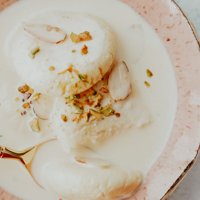 A bowl of Ras Malai dessert topped with pistachios and syrup