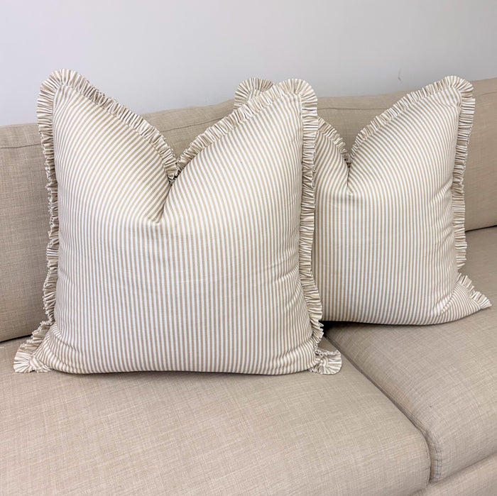 Two striped pillows with ruffled edges on a beige sofa against a light gray wall.