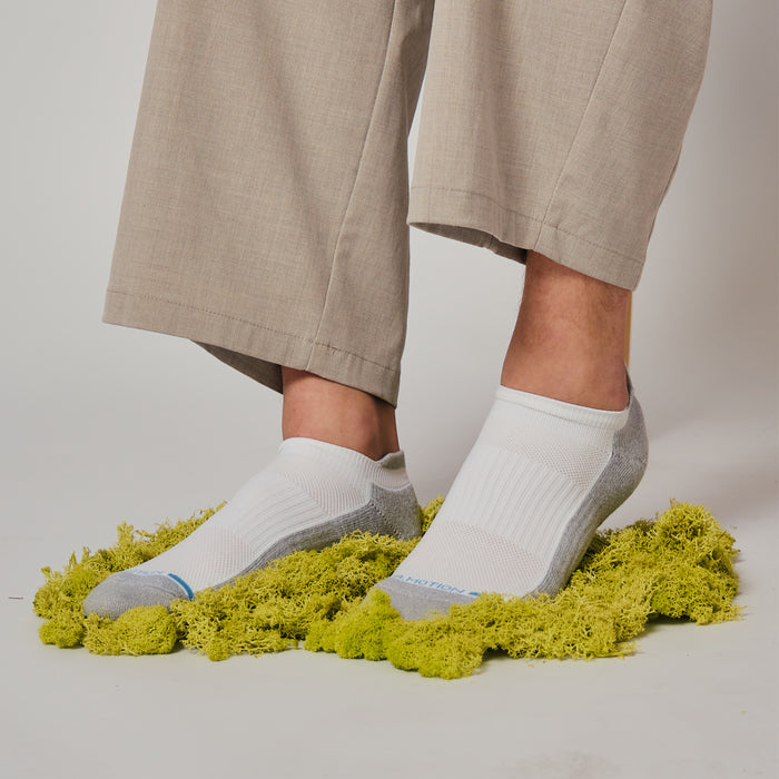 Ankle compression socks in white and gray worn on feet, resting on a bed of green moss.