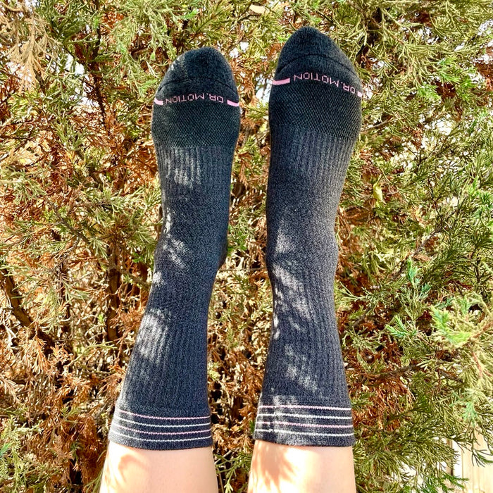 Gray compression crew socks with thin stripes, displayed against a backdrop of greenery.
