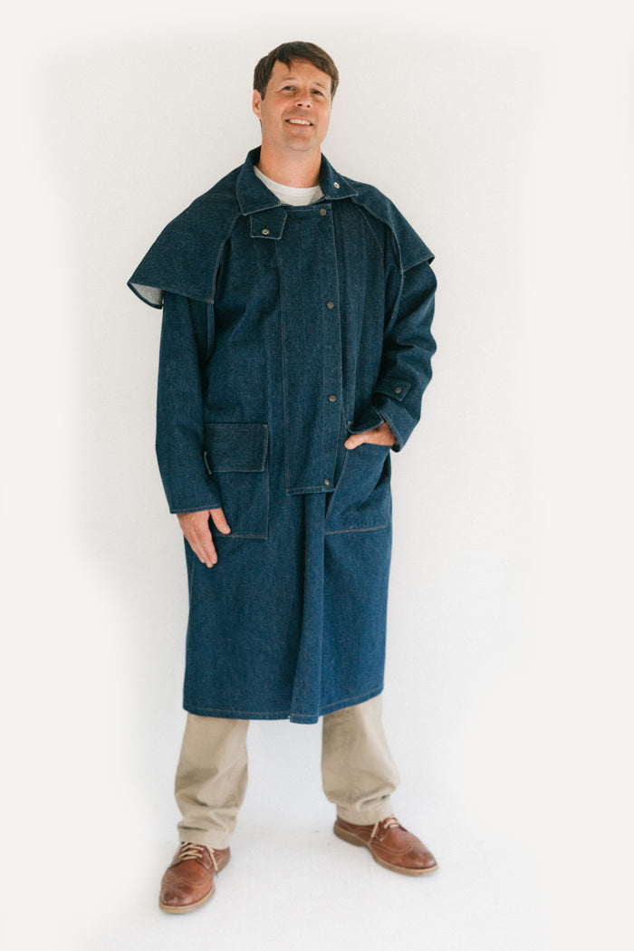 Man standing in front of a white screen wearing a dark blue Drover's Coat.