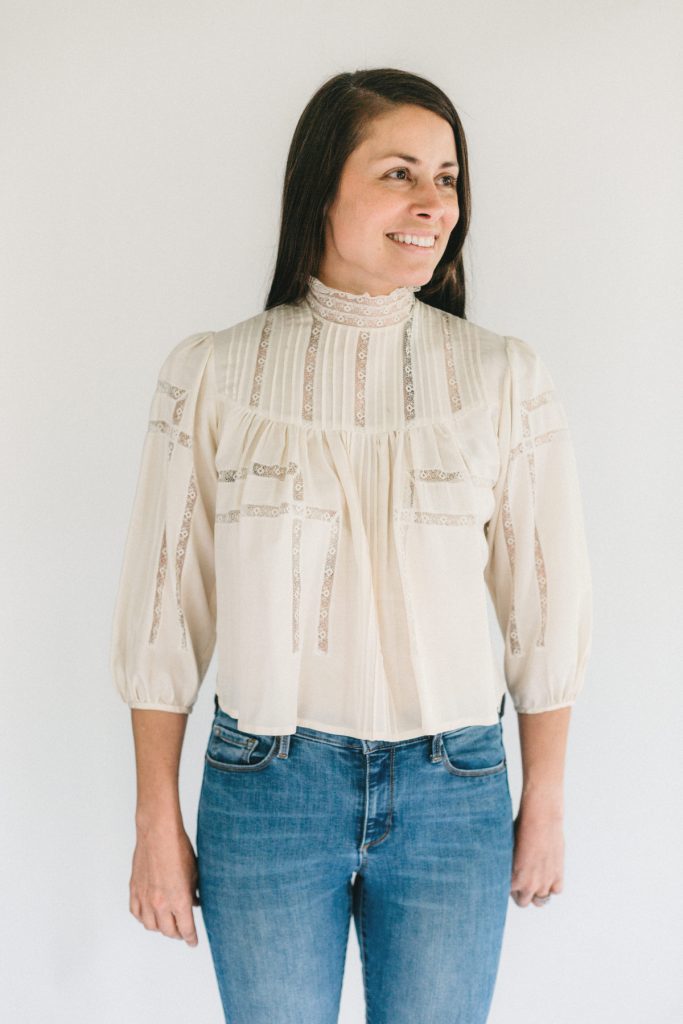 Brunette woman smiling, standing in front of a white studio backdrop wearing 206 Gibson Girl Blouse.