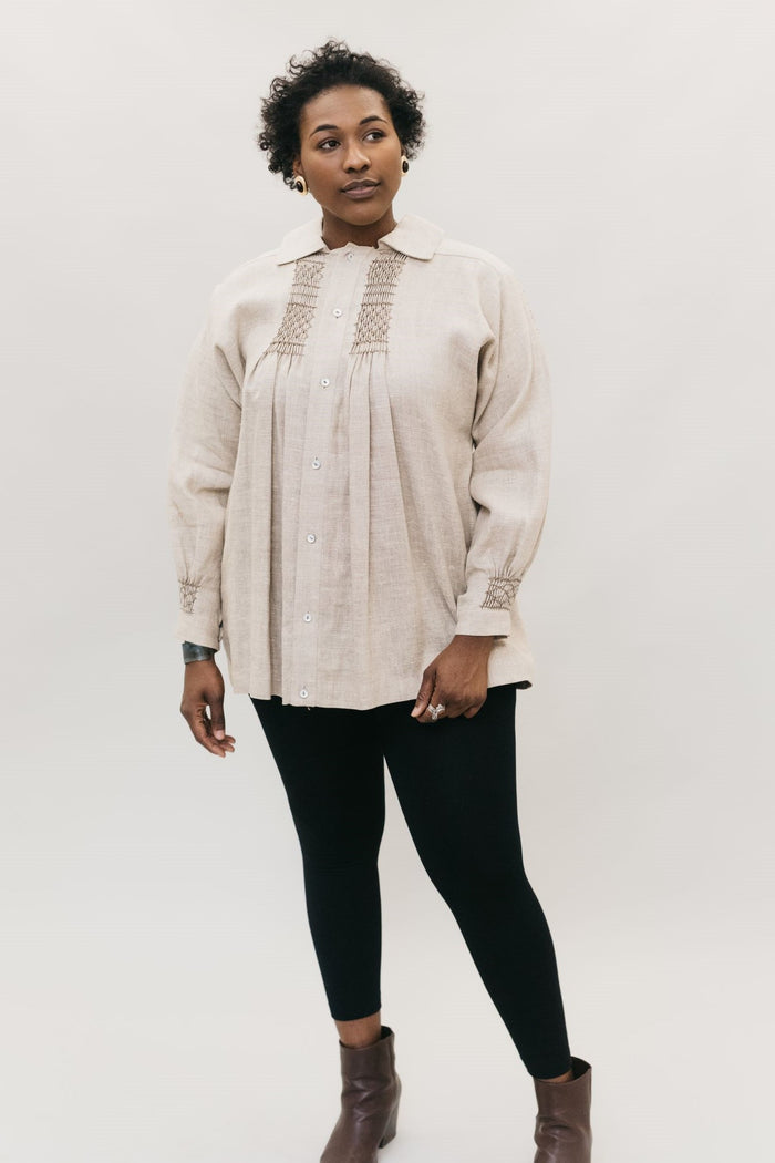 Young African American woman standing in front of a white studio backdrop looking right, wearing 221 English Smock.