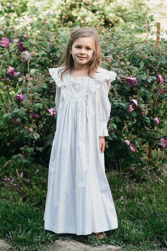 Brunette girl standing in front of Greenery and purple roses. Wearing 225 Childhood Dreams.