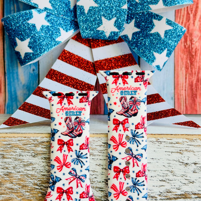 American Girly silicone Apple Watch band with red and blue coquette bows, mini cowboy boots, stars, and "American Girly" script on a white base, shown displayed and worn on Apple Watch against a patriotic 4th of July backdrop.