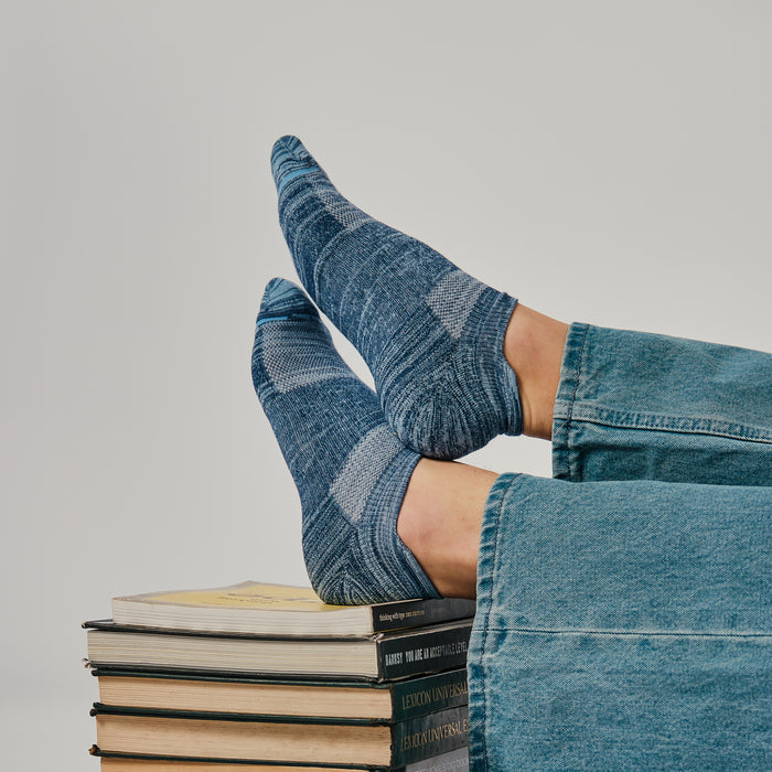 Ankle compression socks in blue tones worn on feet resting on a stack of books.