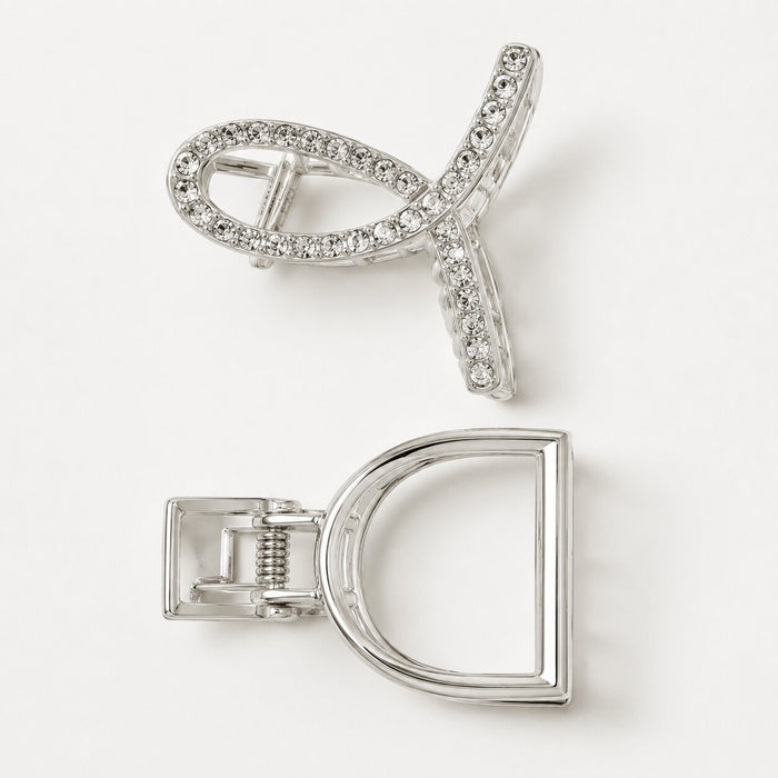 A silver-toned hair claw clip shown from two angles on a clean white background. One view shows the front with a curved open design set with clear rhinestones, and the other shows the back with a D-shaped frame and spring-loaded clasp mechanism.