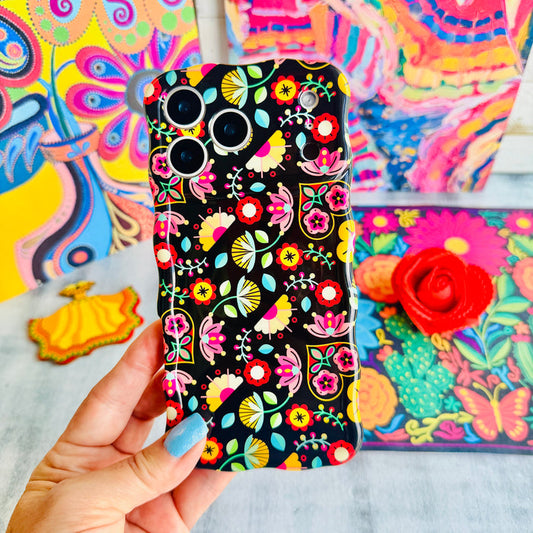 Trendy black wavy iPhone case featuring an intricate folk art botanical pattern of red flowers, magenta details, and yellow fan petals with a high-gloss finish.