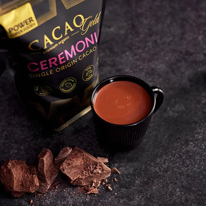 Cacao Gold Ceremonial chocolate product with a cup of chocolate liquid on a dark background