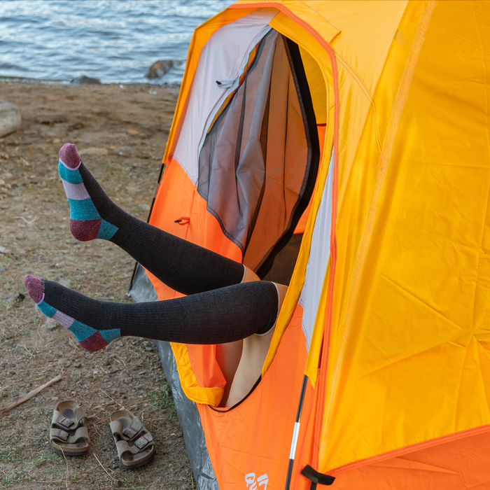 Knee-high socks in color block design, worn by a person sitting in an orange tent by a lakeside.