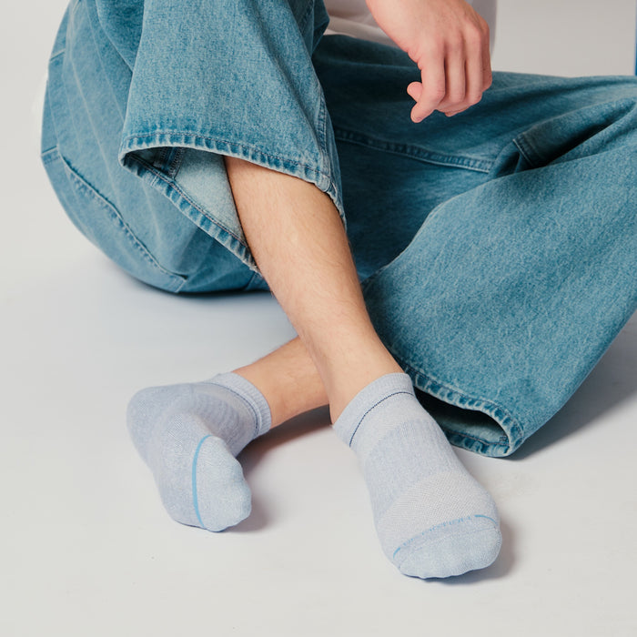 Light blue ankle compression socks with contrast stripes, worn by a person sitting in denim pants.