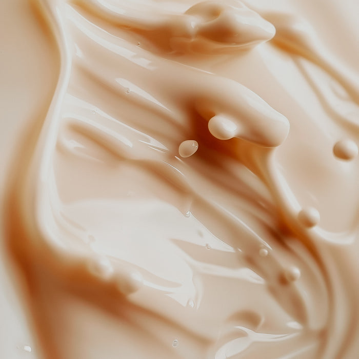 A close-up image of a creamy milk-colored fragrance oil with a smooth texture, showing droplets and ripples.