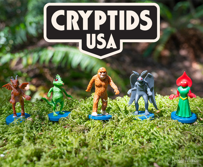 Five cryptid figurines stand on moss under a Cryptids USA sign.