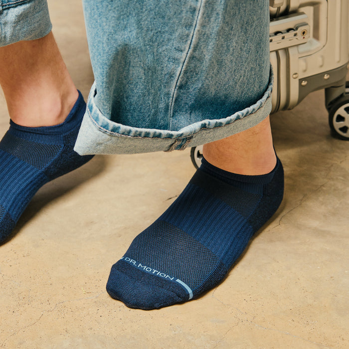 Navy ankle compression socks worn with rolled-up denim pants, next to a silver suitcase on a concrete surface.