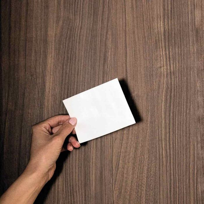 Hand holding a blank white card against a wooden background.
