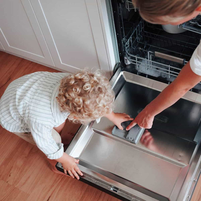 Child and adult interacting with an open dishwasher in a kitchen.