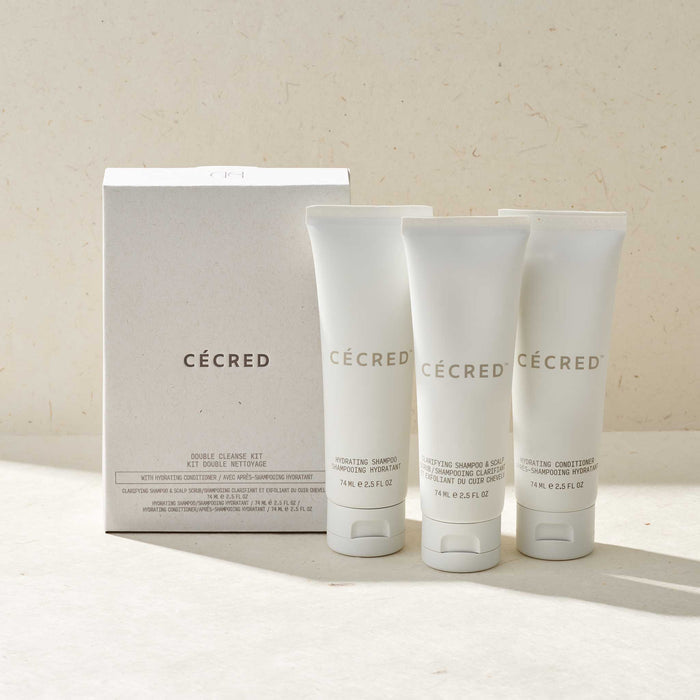 Cécred Double Cleanse Kit with Hydrating Conditioner featuring three travel-size 74ml tubes — Hydrating Shampoo, Clarifying Shampoo & Scalp Dermafoliant, and Hydrating Conditioner — displayed alongside white box packaging on a warm beige surface in soft natural light