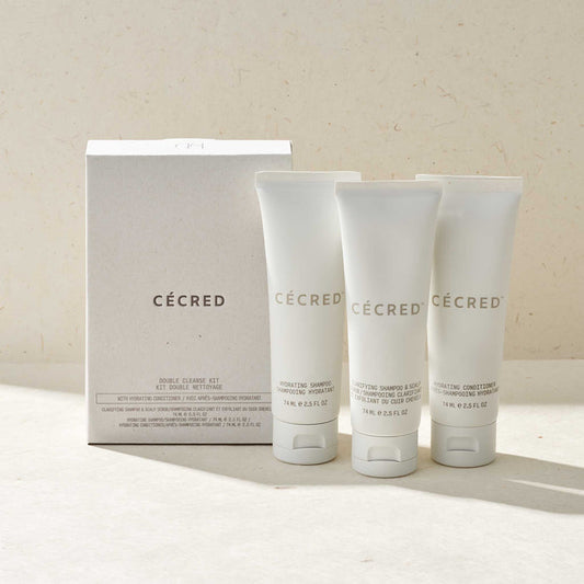 Cécred Double Cleanse Kit with Hydrating Conditioner featuring three travel-size 74ml tubes — Hydrating Shampoo, Clarifying Shampoo & Scalp Dermafoliant, and Hydrating Conditioner — displayed alongside white box packaging on a warm beige surface in soft natural light