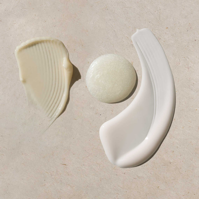 Three product texture swatches from the Cécred Double Cleanse Kit with Hydrating Conditioner displayed on a warm beige surface — a ridged shampoo smear, a round scalp dermafoliant dollop, and a smooth conditioner swipe showcasing each formula's consistency