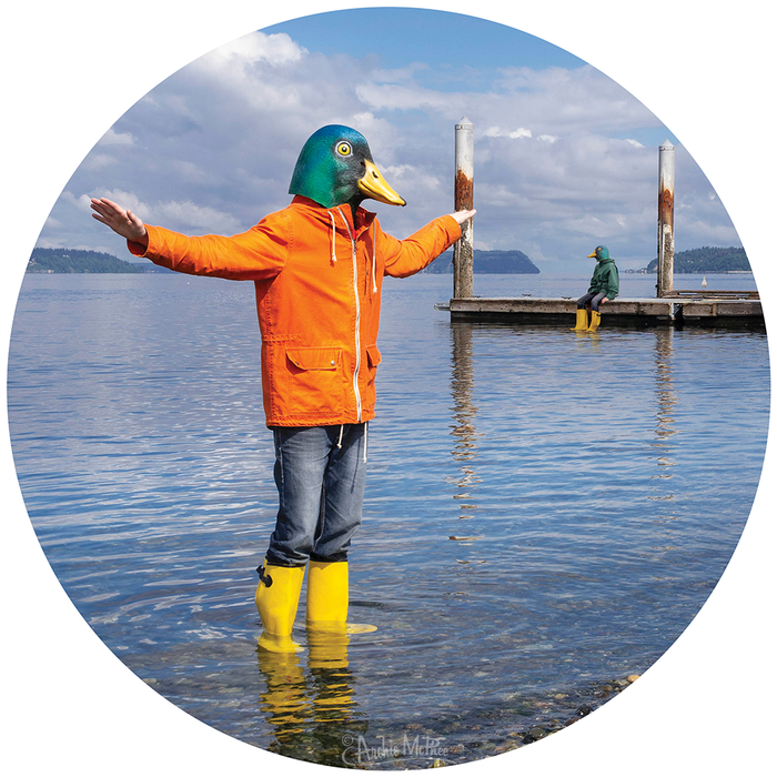 A person in a duck mask, orange jacket, and yellow boots stands in the water with outstretched arms, capturing the joy of the "Duck Day Afternoon Puzzle." Another sits thoughtfully on the dock nearby.