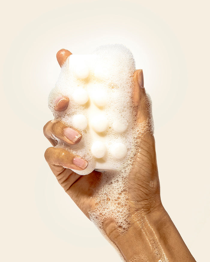 Hand holding a foamy bath bomb against a plain background