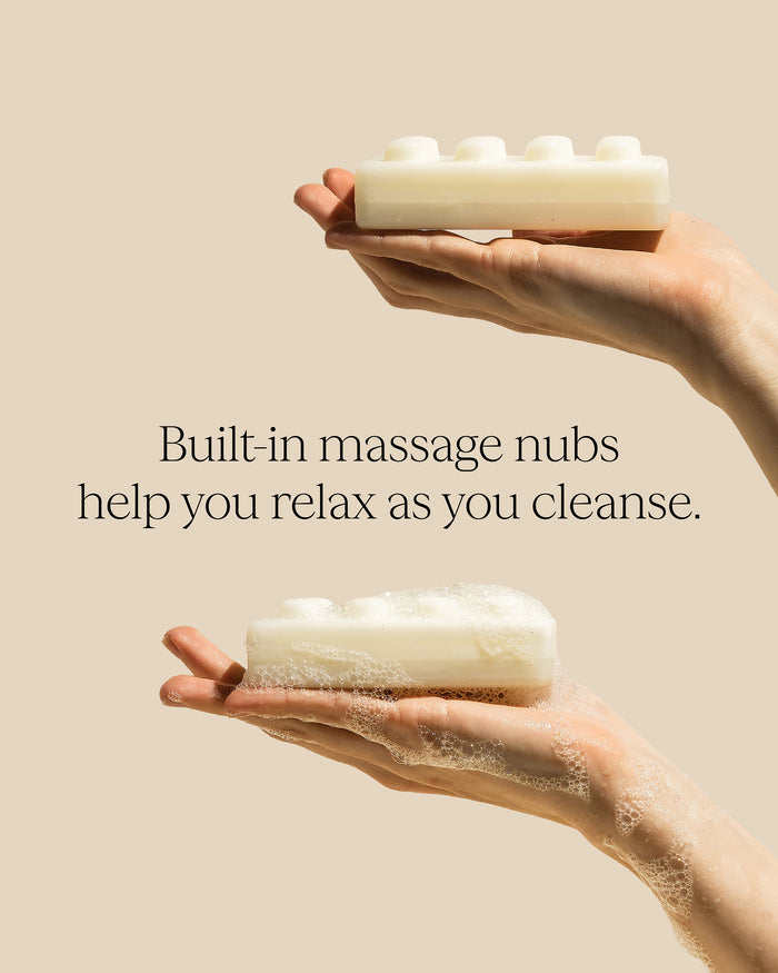 Hands holding a bar of soap with built-in massage nubs against a beige background