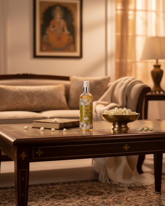 Indian Mogra room fragrance bottle on a wooden table beside scattered blossoms.