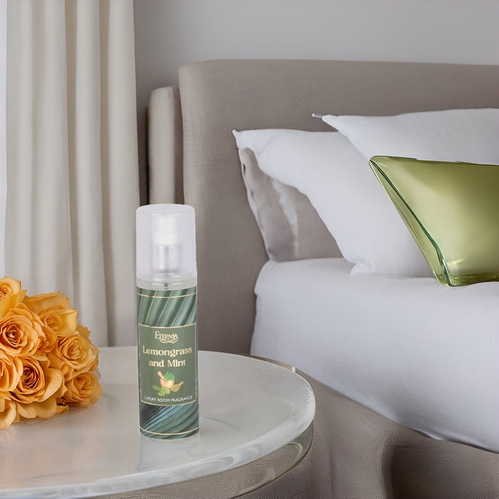 Luxury room spray bottle with white cap on a bedside table near pillows and flowers