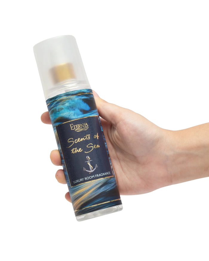Luxury room spray bottle held in hand, white cap and blue wave label.