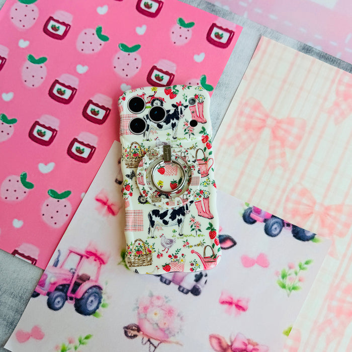 Farm Girl Cutie Wavy Luxe iPhone case with the matching MagSafe grip ring attached, styled on pink strawberry and tractor print paper.