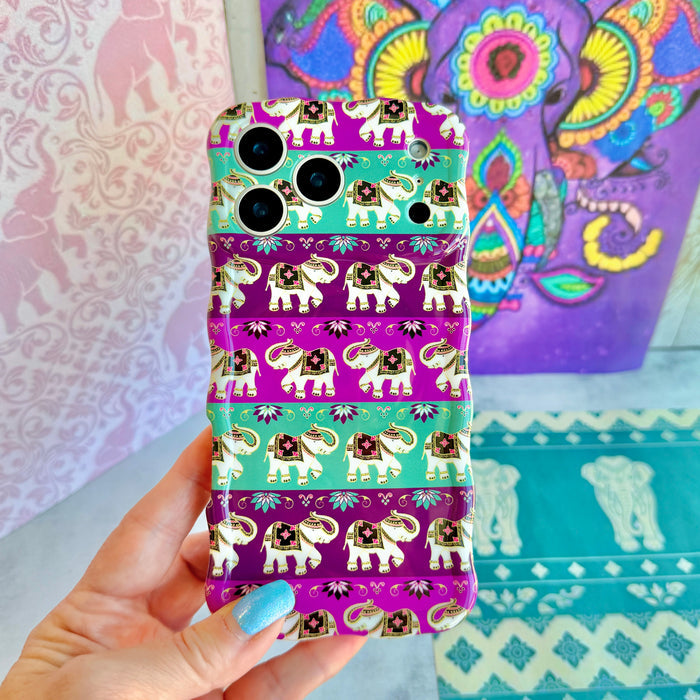 Hand holding the Fortune Parade Wavy Luxe MagSafe iPhone case, showing the purple and teal striped print with decorated boho elephants.