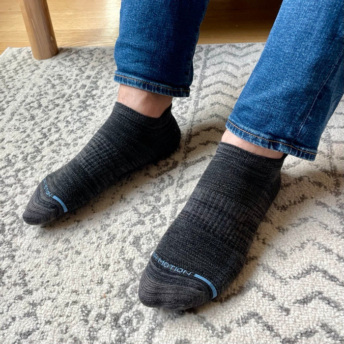 Ankle compression socks in dark gray worn with blue jeans, resting on a patterned rug.