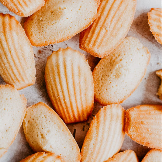 A close-up image of French Madeleines, which are small, sponge cakes with a distinctive ribbed texture and golden-brown edges.