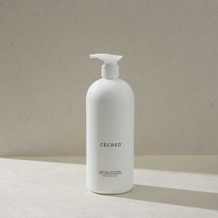 Cécred Hydrating Conditioner in the max size pump bottle, standing on a beige surface against a tan textured background