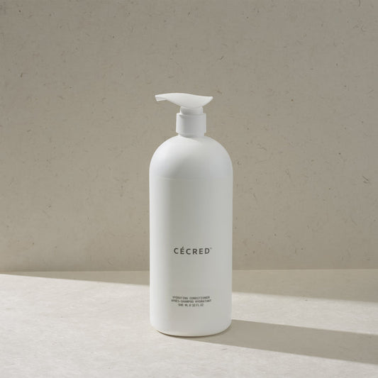 Cécred Hydrating Conditioner in the max size pump bottle, standing on a beige surface against a tan textured background