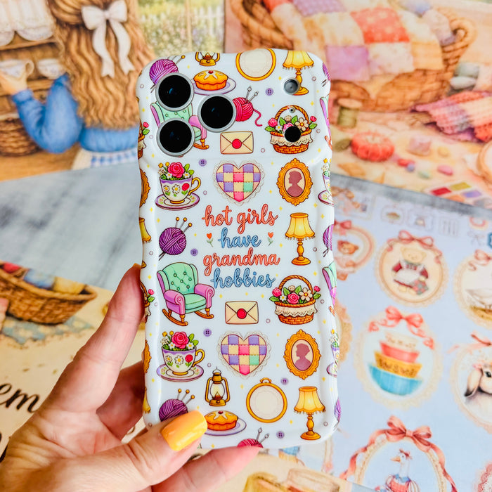 Hand holding the It's Giving Grandma Hobbies Wavy Luxe MagSafe iPhone case, showing the cream print with teacups, embroidery hoops, lamps and hot girls have grandma hobbies lettering.