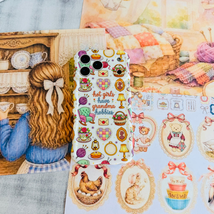 It's Giving Grandma Hobbies Wavy Luxe MagSafe iPhone case styled against a cottage sitting room illustration with a bow and cross-stitch motifs.