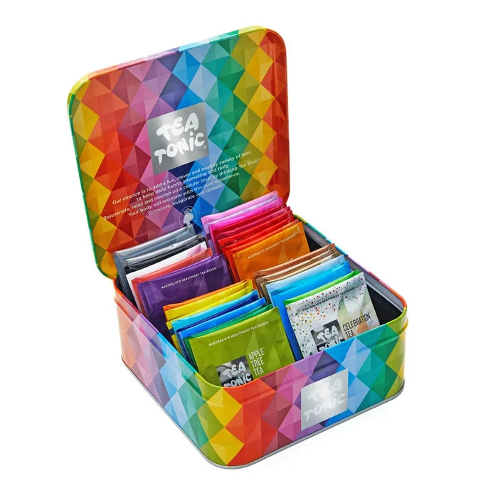 A colourful geometric-patterned metal tea tin shown open, filled with assorted tea bags in bright assorted colours. The brand name 'Tea Tonic' is visible on the inner lid and on several tea bags.