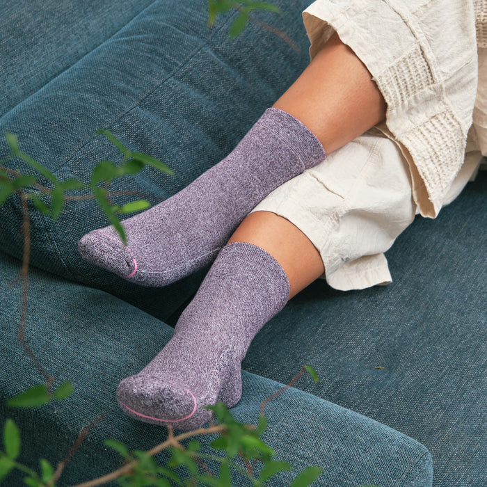 Purple half-cushion socks with a pink accent, worn on feet resting on a teal couch.