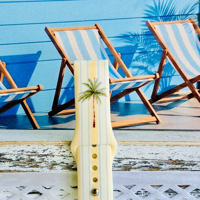 Palm Shore Club silicone Samsung Watch band with hand-painted palm trees over soft blue and yellow cabana stripes on an ivory base, shown displayed and worn on Apple Watch against a coastal beach club backdrop.