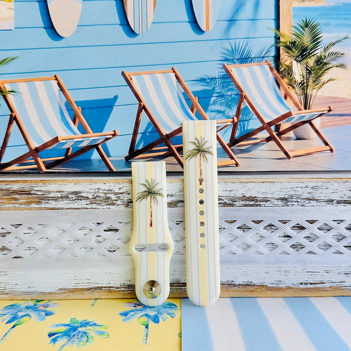 Palm Shore Club silicone Samsung Watch band with hand-painted palm trees over soft blue and yellow cabana stripes on an ivory base, shown displayed and worn on Apple Watch against a coastal beach club backdrop.