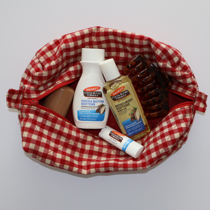 Red and white checkered bag with Palmers Cocoa Butter travel products on a light gray background