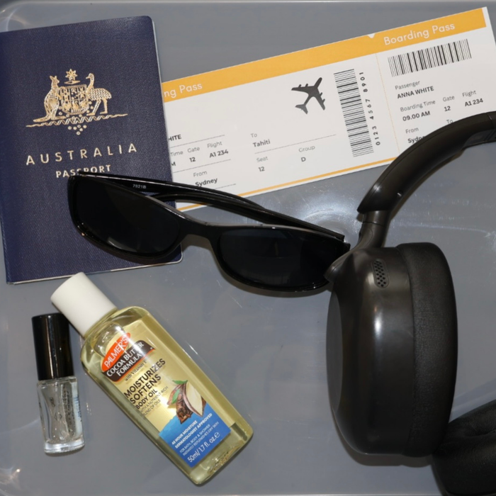 Australian passport, sunglasses, boarding pass, and travel-sized Palmer's Cocoa Butter Body Oil on a gray surface