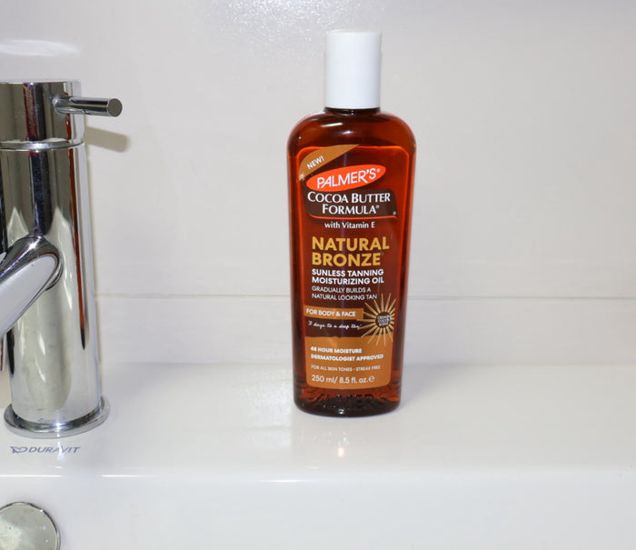 Bottle of Palmer's Cocoa Butter Formula Natural Bronze Sunless Tanning Moisturizing Oil on a bathroom counter.