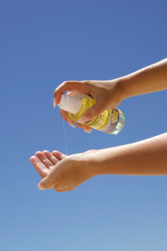Hand applying Palmer's Tahitian Vanilla Body Oil into hands against a clear blue sky